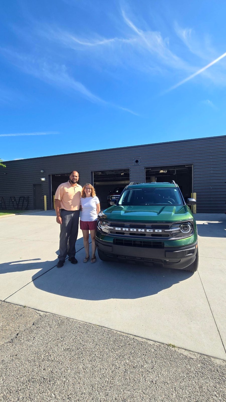 Amy and her Friendly Ford sales consultant standing beside her new green 2024 Ford Bronco Sport