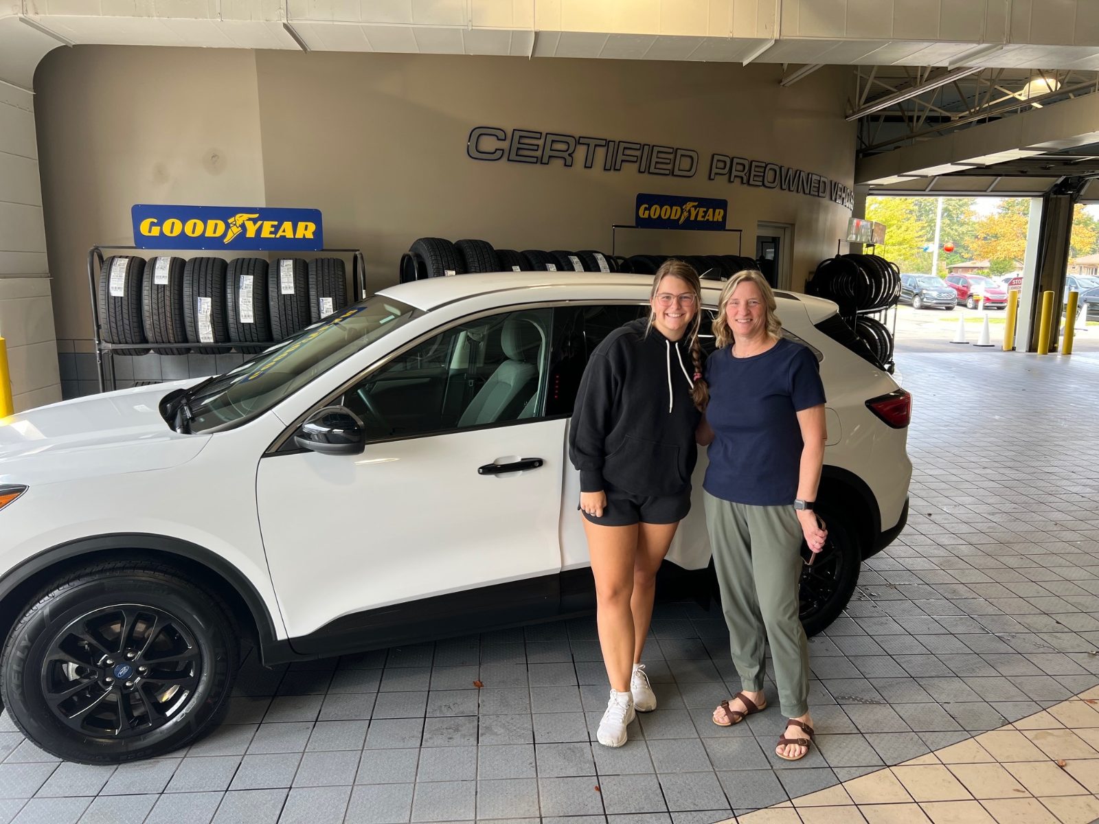 Britney and a Friendly Ford team member standing beside her white 2020 Ford Escape in the dealership's certified pre-owned bay