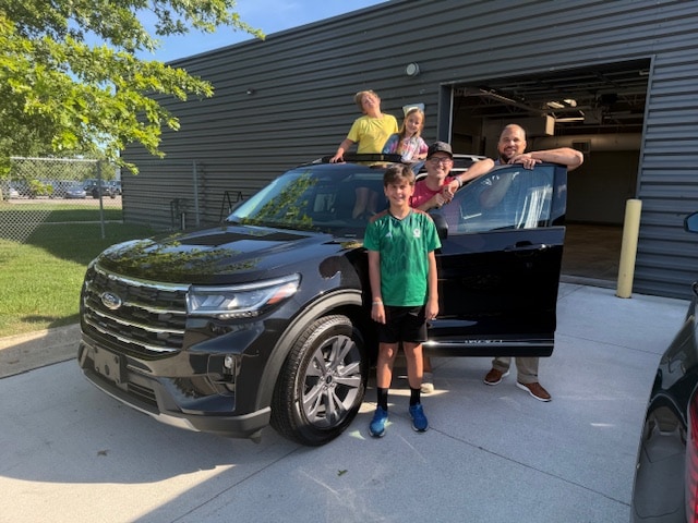 Charles and his children with their new 2025 Ford Explorer Active in Agate Black, two of the children looking out through the panoramic sunroof