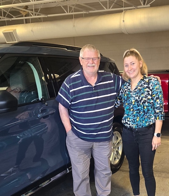 David and his Friendly Ford sales consultant standing beside his new dark blue 2025 Ford Explorer