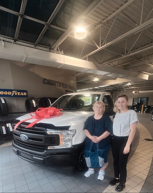 Kathy and her Friendly Ford salesperson beside her 2019 Ford F-150, topped with a large red bow in the showroom