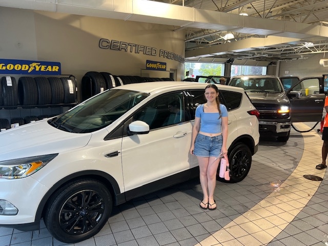Olivia standing beside her white 2019 Ford Escape in the Friendly Ford certified pre-owned bay