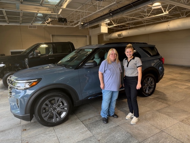 Priscilla and her Friendly Ford salesperson beside her new 2025 Ford Explorer AWD Active in Vapor Blue
