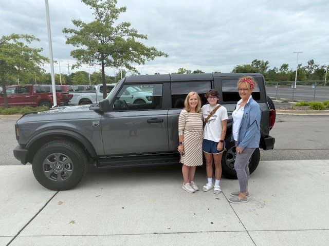 Three people standing beside Renee's new gray Ford Bronco Big Bend outside Friendly Ford