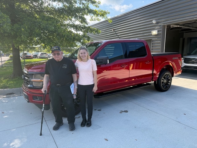 Thomas and his Friendly Ford salesperson standing beside his new red Ford F-150 XLT