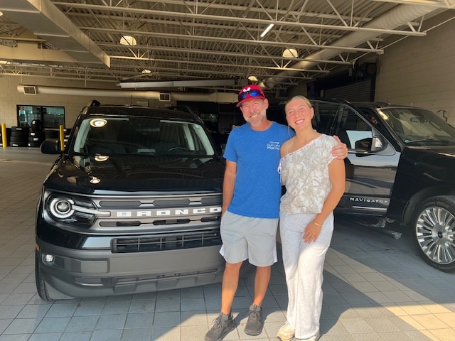Two members of the Willis family standing beside their 2022 Ford Bronco Sport in the Friendly Ford delivery bay
